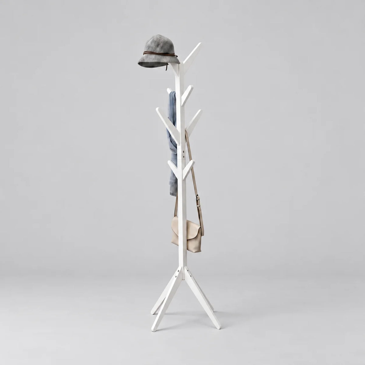 Porte-manteau arbre en bois peint blanc à huit crochets et pieds évasés, avec chapeau gris, écharpe bleu gris et sac beige, sur fond gris
