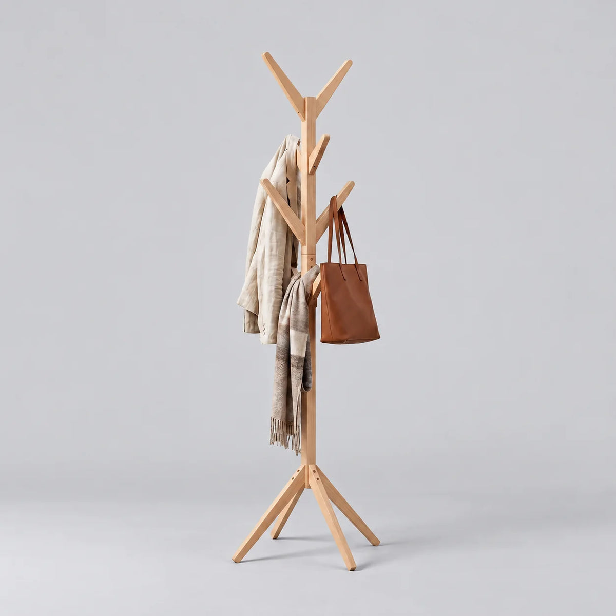 Porte-manteau arbre en bois clair à huit crochets et base évasée, avec manteau beige, écharpe et sac cognac, sur fond gris