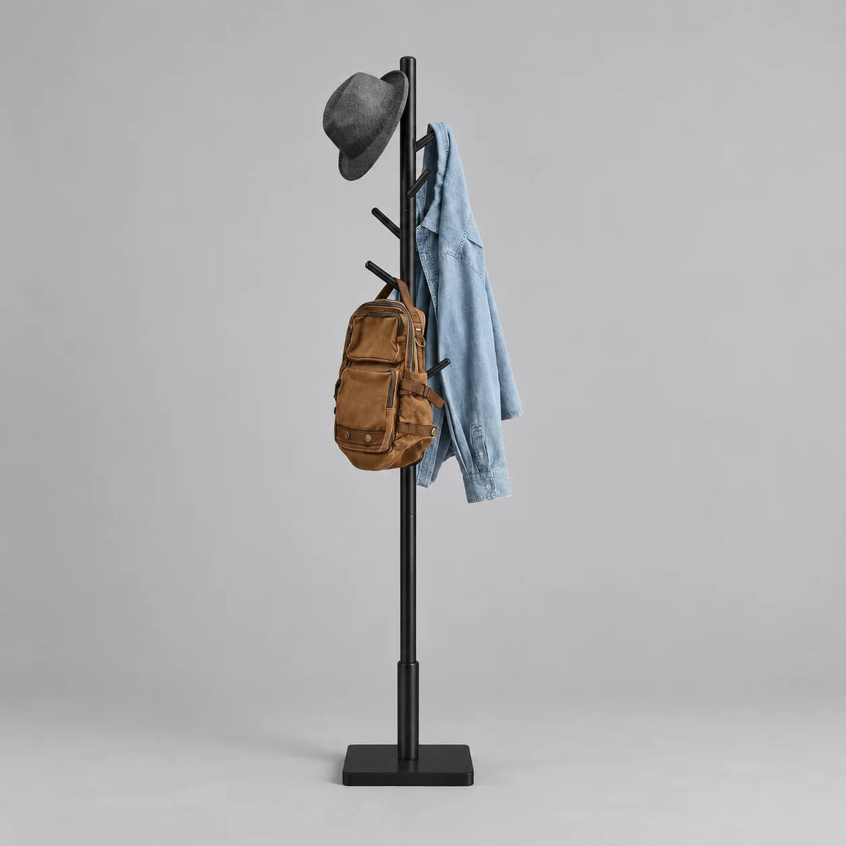 Porte-manteau arbre en bois noir à huit crochets avec chapeau gris, veste en jean et sac brun sur fond gris Image