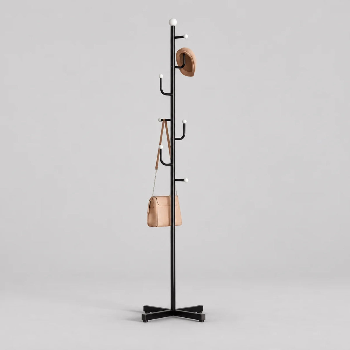Porte-manteau noir sur pied à embouts blancs et base croisée avec chapeau et sac sur fond gris