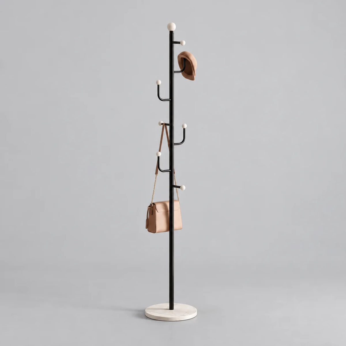 Porte-manteau noir sur pied à embouts blancs et base ronde blanche veinée avec chapeau et sac sur fond gris Image