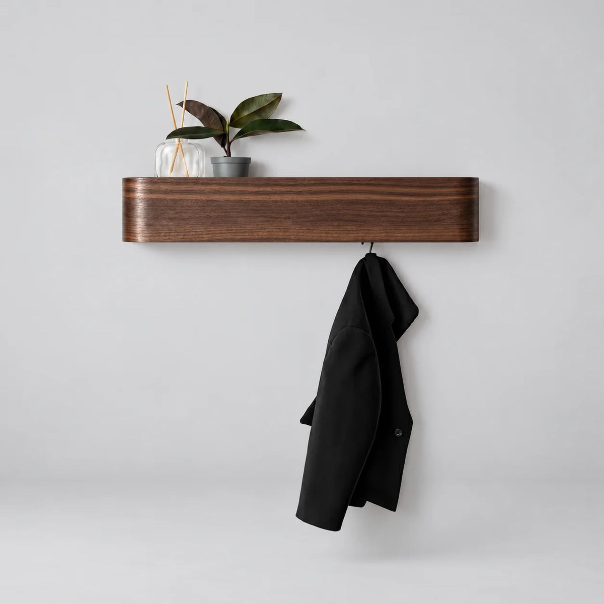 Porte-manteau mural en bois foncé façon noyer à façade rectangulaire arrondie, avec diffuseur, plante et manteau noir, sur fond gris