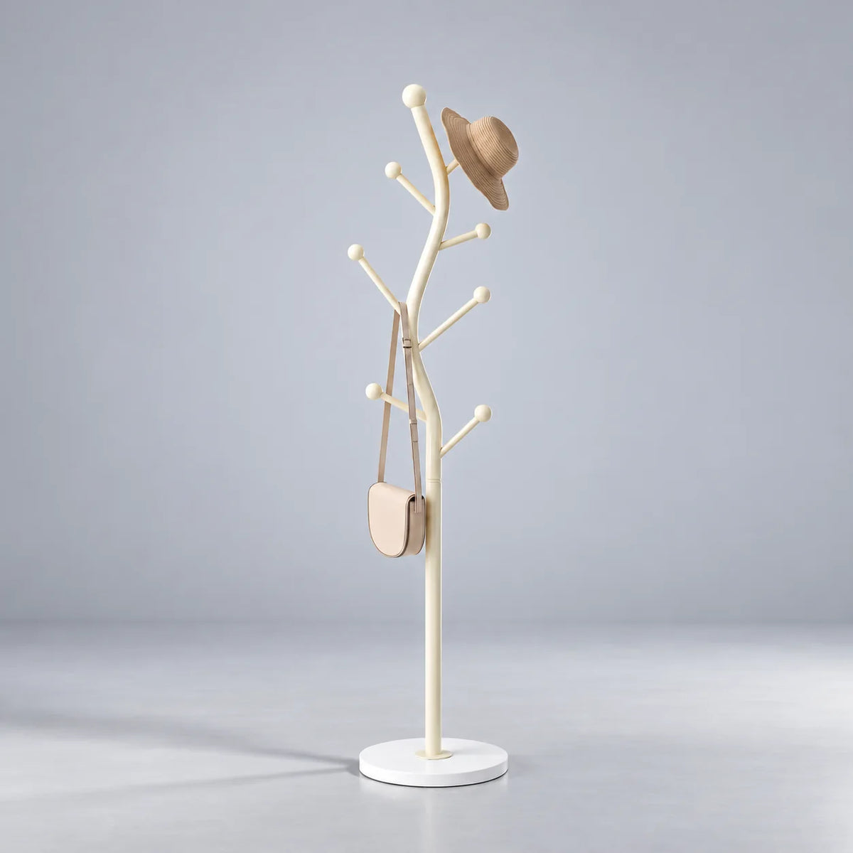 Porte-manteau arborescent en acier blanc crème à sept embouts ronds, pied circulaire blanc, chapeau de paille beige et petit sac crème sur fond gris