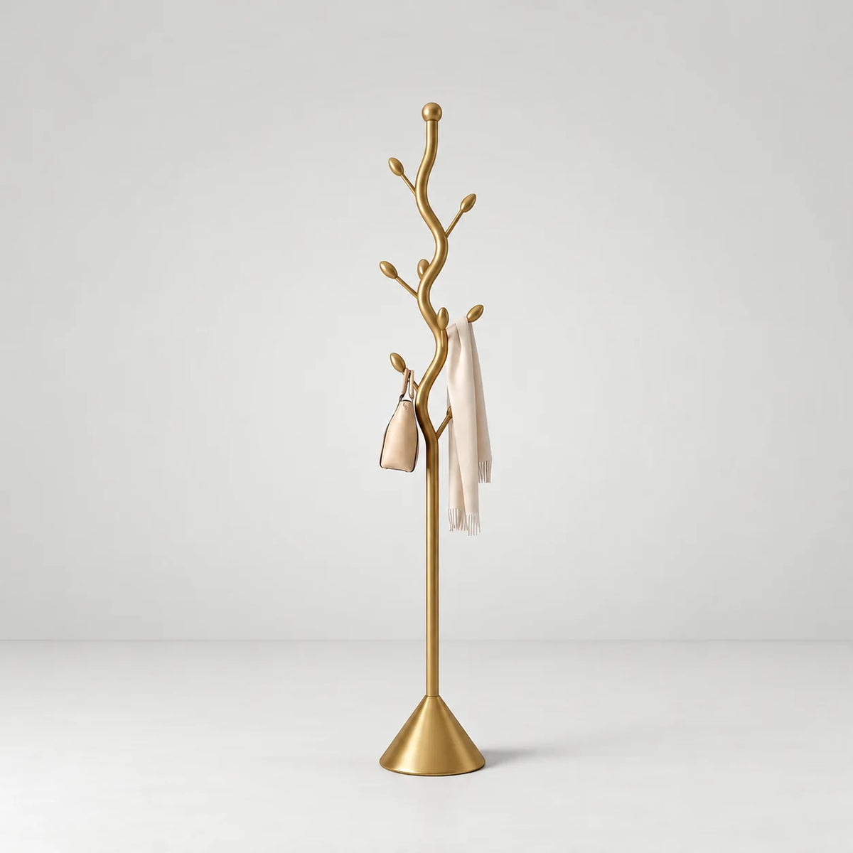 Porte-manteau arborescent en acier doré brossé avec branches à embouts dorés, base conique, sac beige et écharpe ivoire sur fond gris