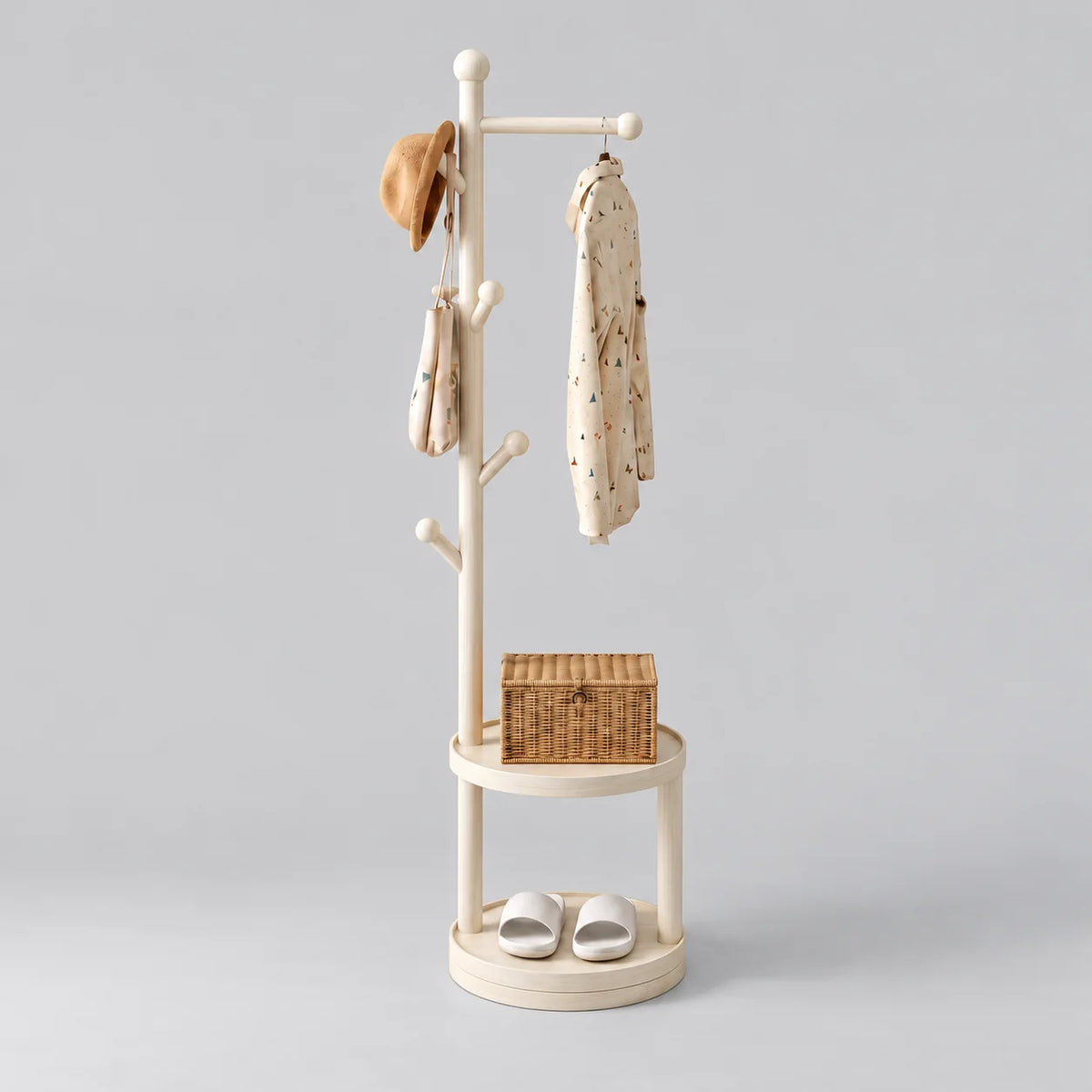 Porte-manteau sur pied en bois blanc, traverse et patères à boules, deux étagères rondes avec panier et chaussures, sur fond gris