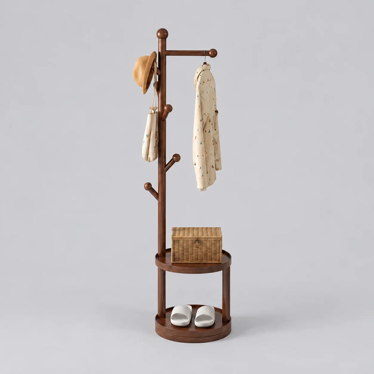 Porte-manteau sur pied en bois marron foncé, traverse et patères à boules, deux étagères rondes avec panier et chaussures, sur fond gris
