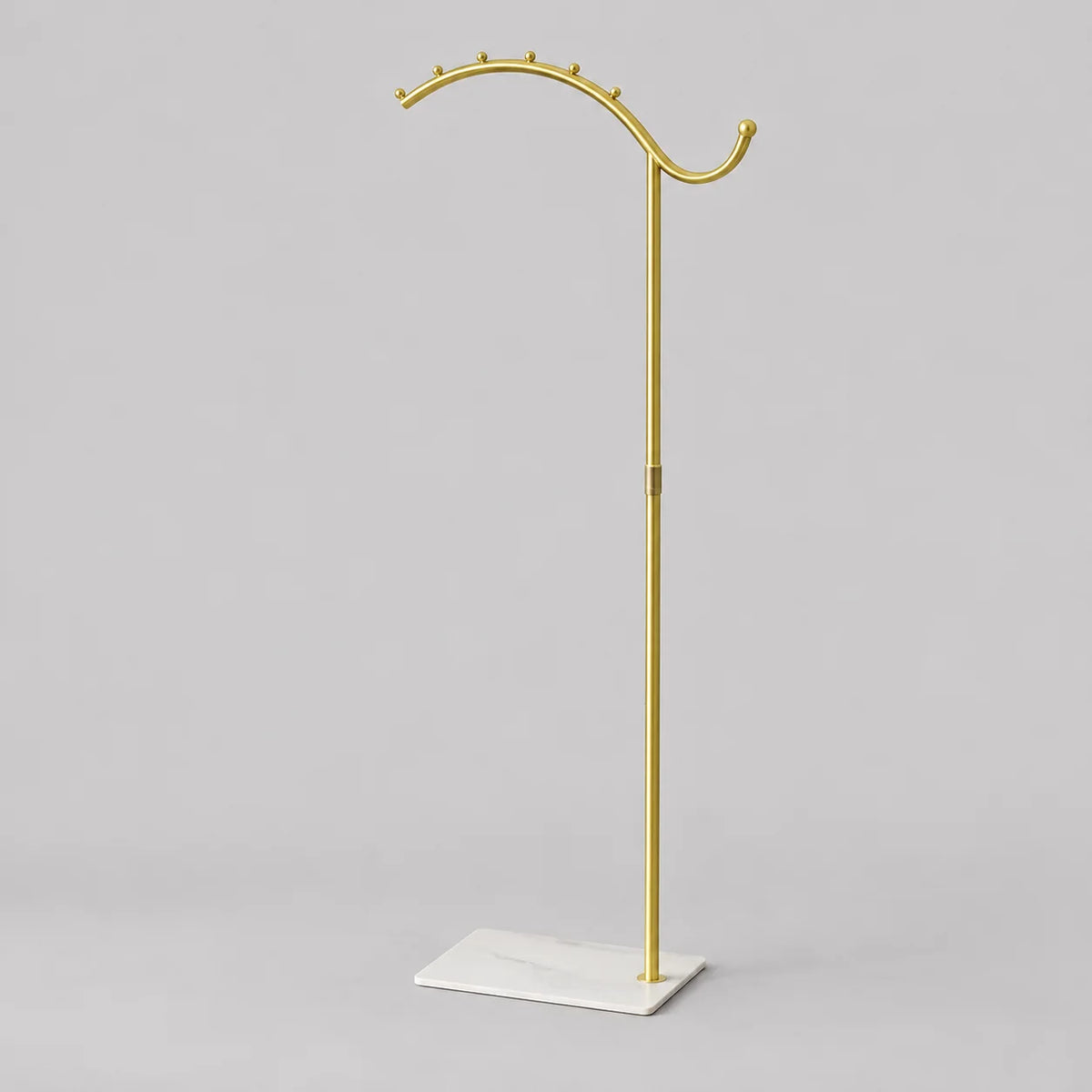 Porte-manteau sur pied voûté, tige dorée et socle blanc, vue complète sur fond gris