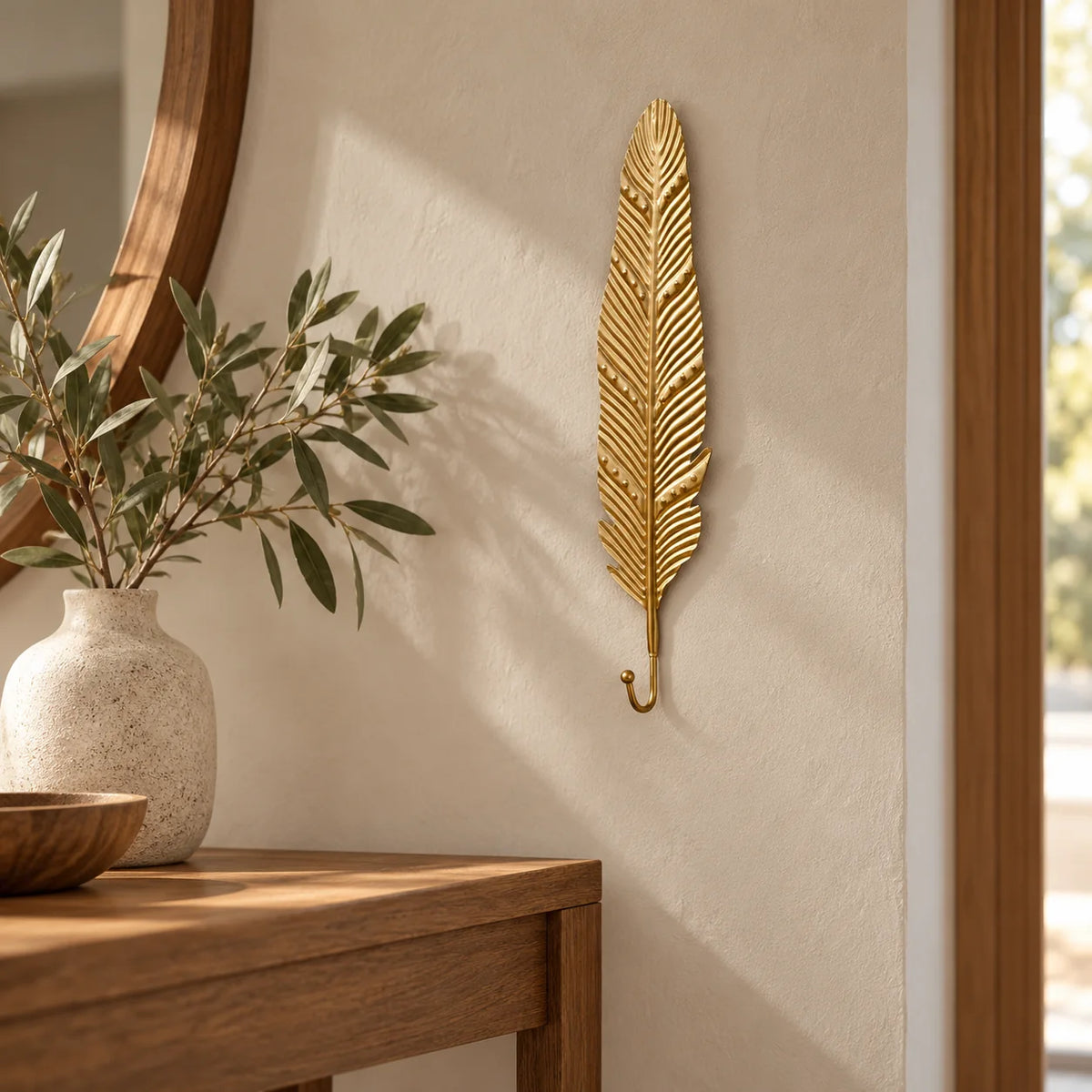 Patère longue feuille dorée installée dans une entrée sur un mur beige