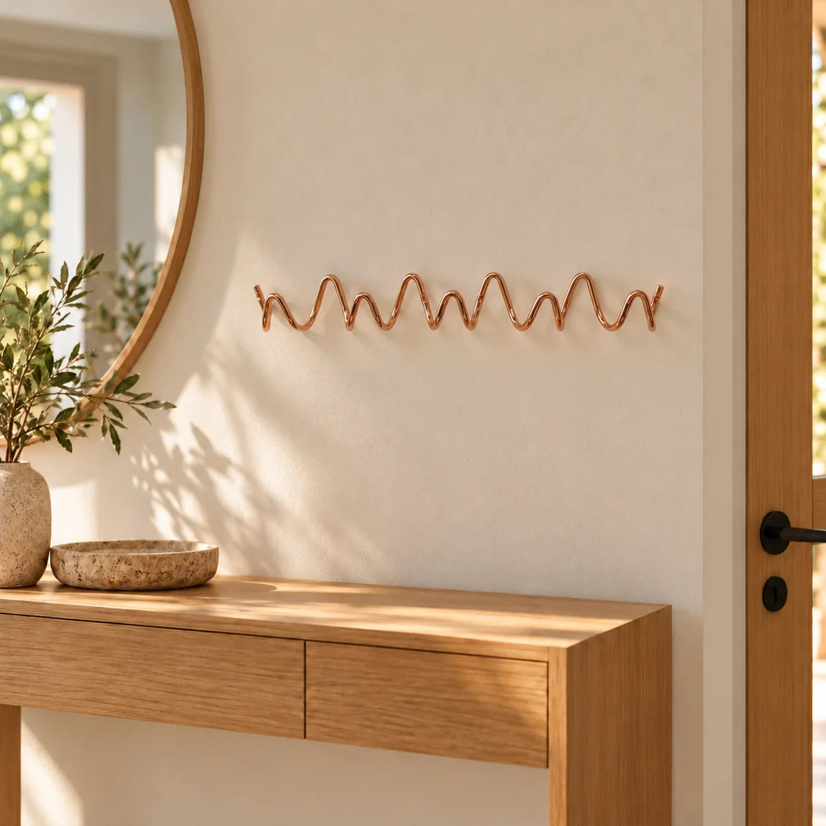 Porte-manteau mural Vrille rose cuivré de 54 cm installé au-dessus d’une console dans une entrée