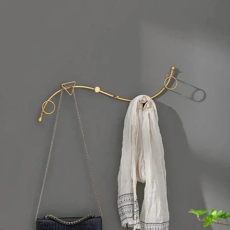 Porte-manteau mural Serpent doré avec sac et écharpe sur un mur gris
