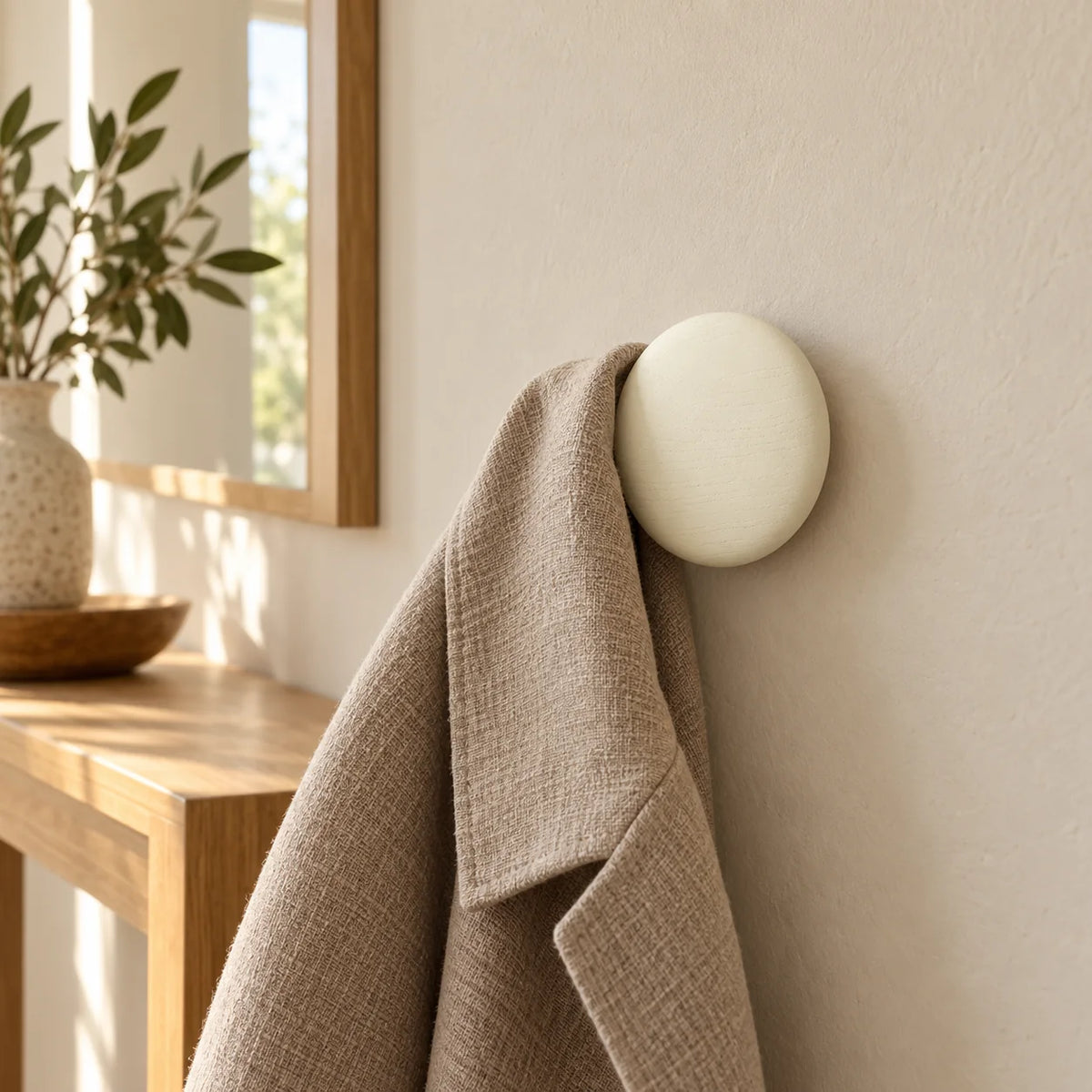 Patère ronde blanche portant une veste dans une entrée