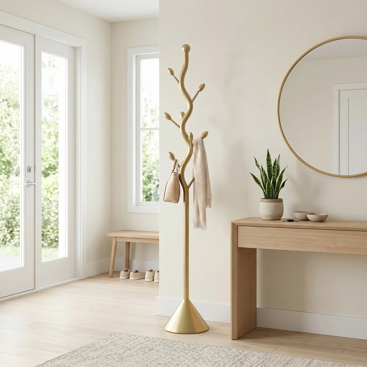 Porte-manteau doré à tronc sinueux et base conique dans une entrée lumineuse, avec sac beige et écharpe ivoire