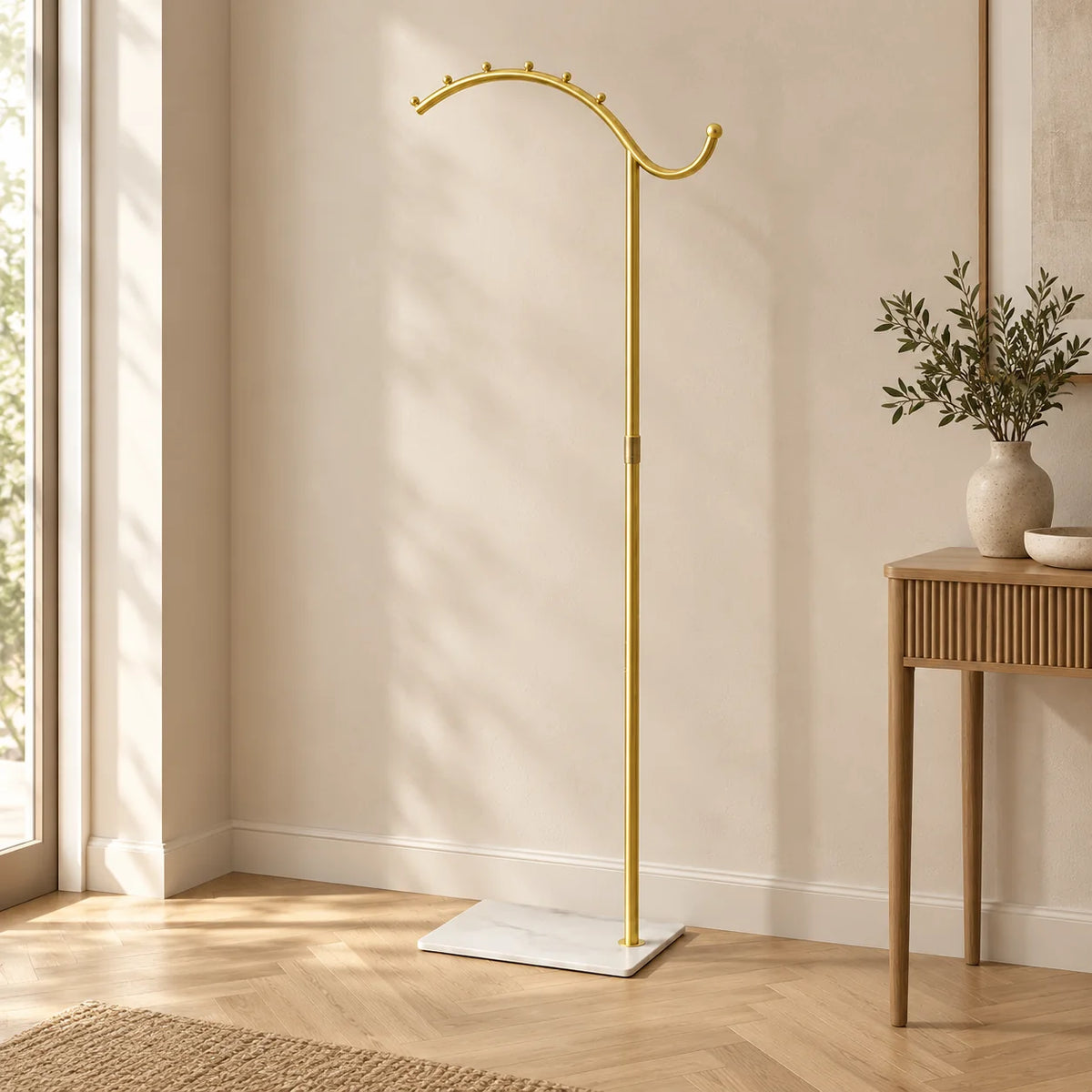 Porte-manteau voûté doré à socle blanc dans une entrée lumineuse, entièrement visible