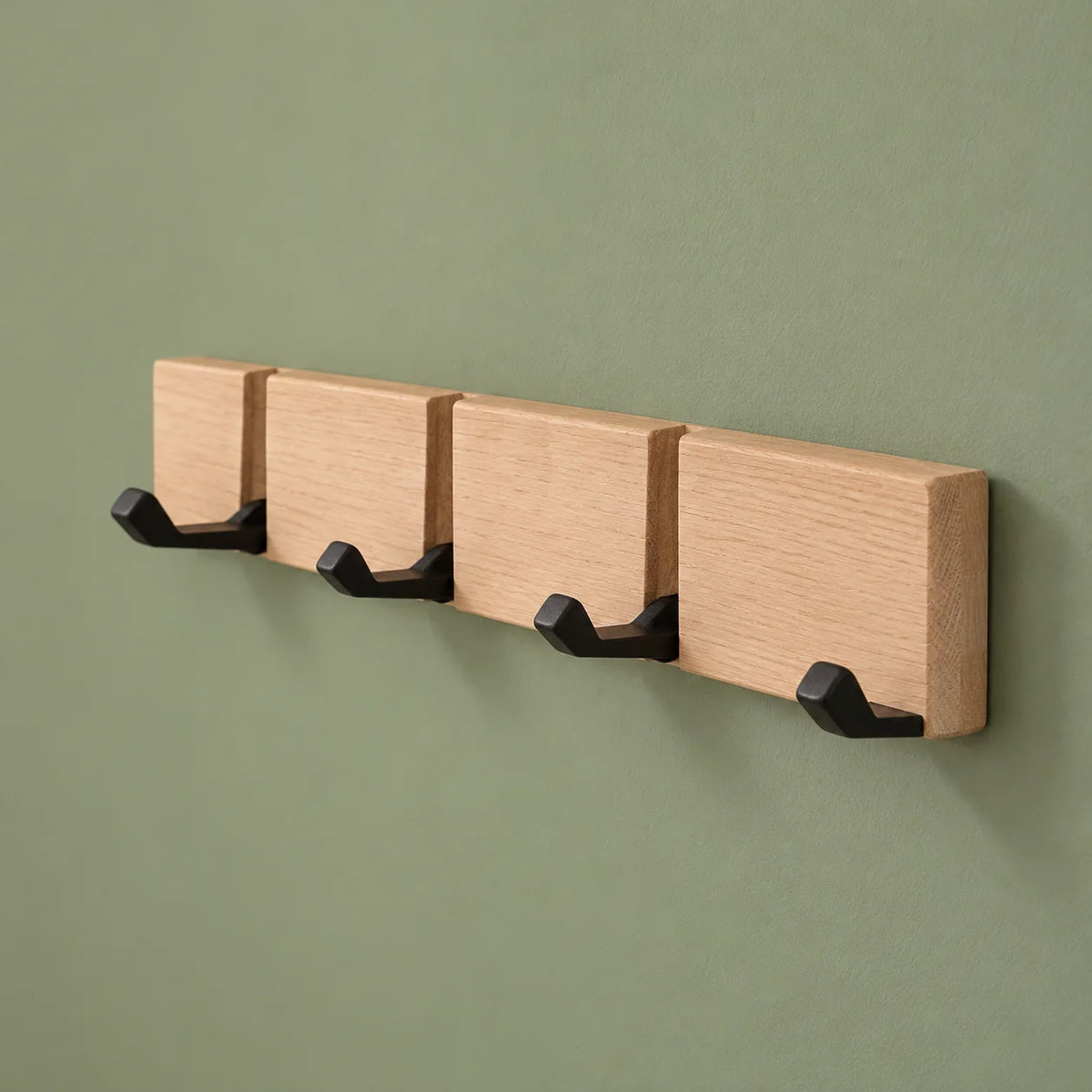 Vue de trois quarts du porte-manteau mural en bois beige à quatre crochets sur fond vert sauge