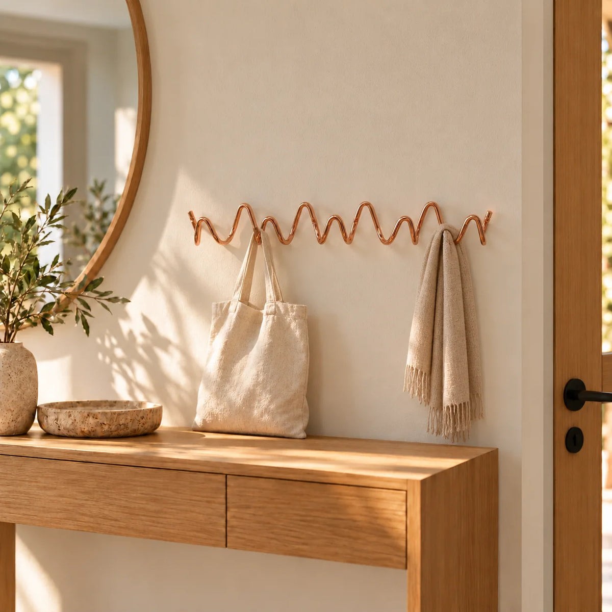 Porte-manteau mural Vrille rose cuivré portant un sac en toile et une écharpe dans une entrée