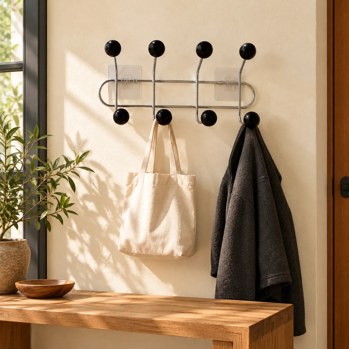 Porte-manteau mural chromé à quatre bras noirs avec sac et veste dans une entrée