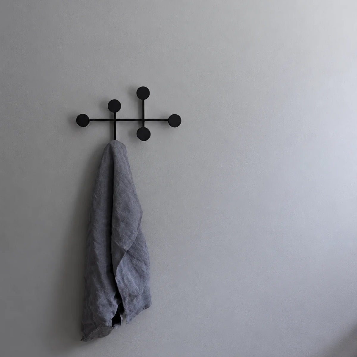 Porte-manteau mural noir à six patères rondes installé sur un mur gris avec écharpe