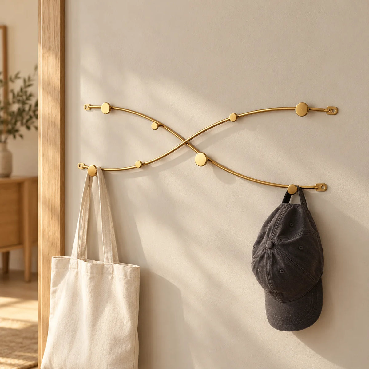 Porte-manteau vague croisée doré fixé dans une entrée, avec sac en toile et casquette