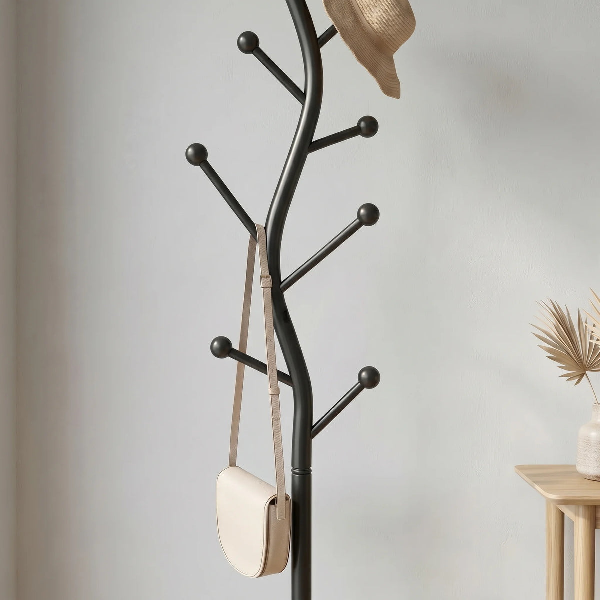 Gros plan sur les branches à embouts ronds du porte-manteau noir mat, avec chapeau beige et sac crème dans une entrée