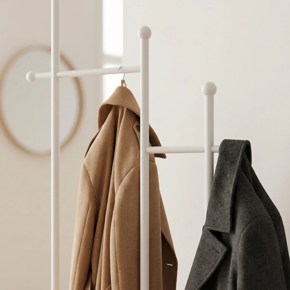 Vue rapprochée du porte-manteau blanc avec montants et traverses à embouts sphériques, manteaux camel et gris suspendus
