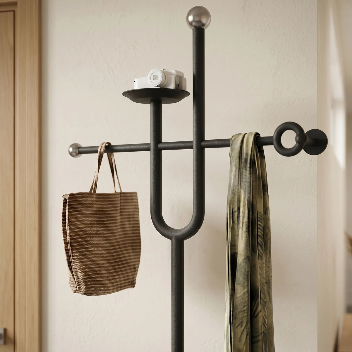 Vue rapprochée de la traverse noire, tablette ronde, branche en U et embouts métalliques du porte-manteau avec sac et écharpe