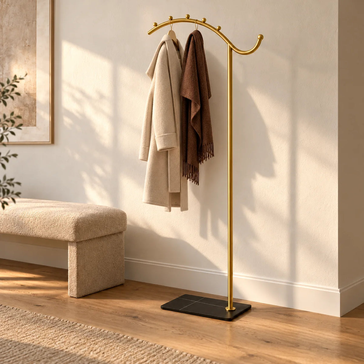 Porte-manteau voûte dorée à socle noir portant un manteau beige et une écharpe
