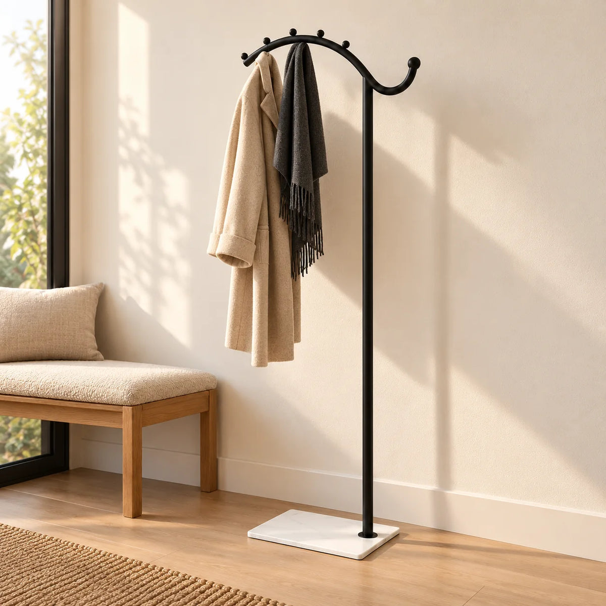 Porte-manteau voûté noir à socle blanc portant un manteau beige et une écharpe