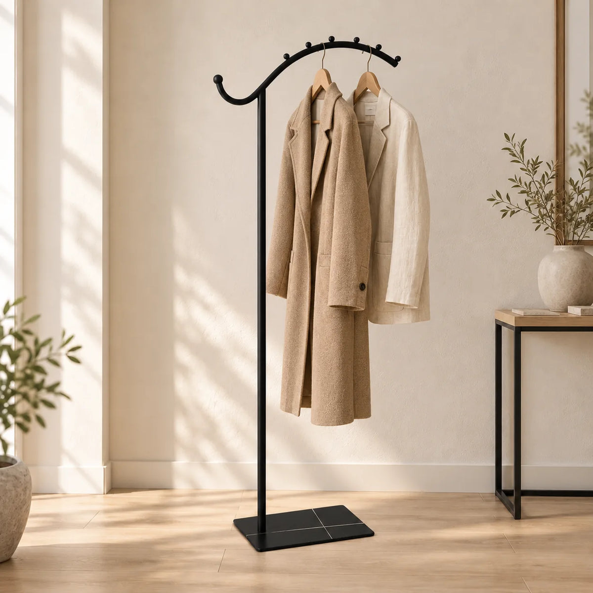 Porte-manteau voûté noir portant un manteau beige et une veste claire dans une entrée