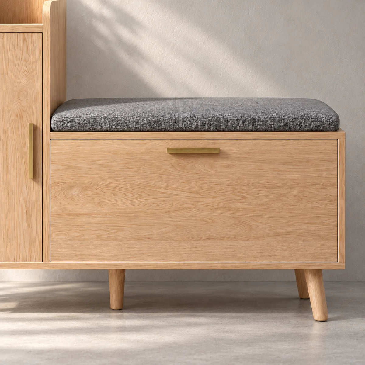 Détail du coussin gris et du coffre à chaussures en bois clair avec poignée dorée