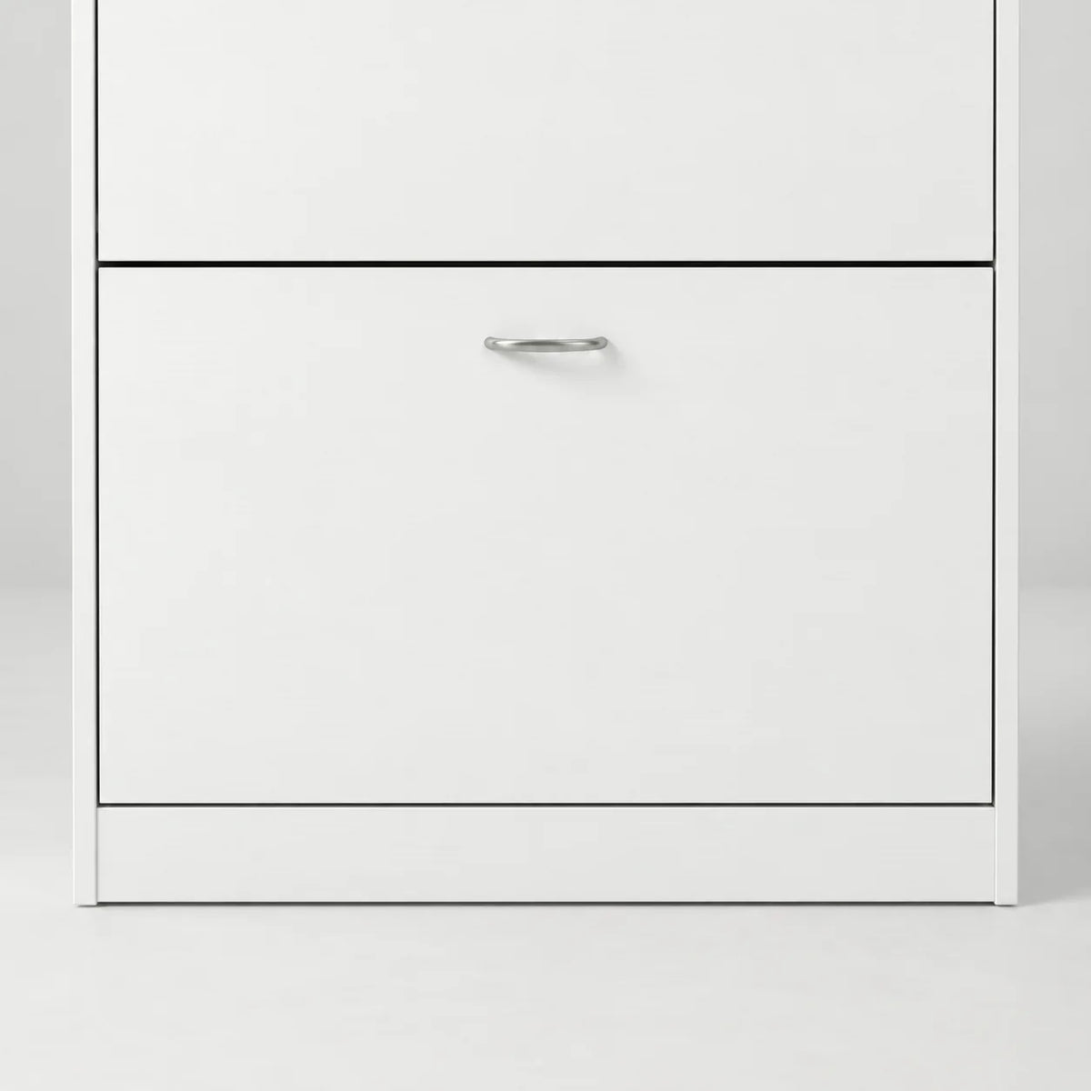 Détail de la porte basse du meuble à chaussures blanc, de sa poignée argentée et du socle plein