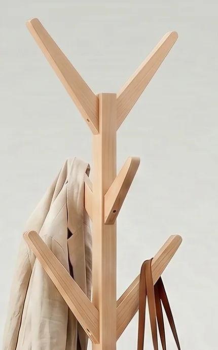 Détail des branches hautes en bois clair et du manteau beige suspendu