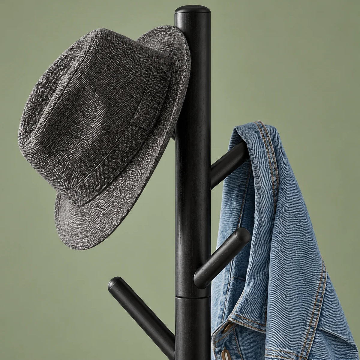 Détail des branches noires supérieures portant un chapeau gris et une veste en jean sur fond vert sauge