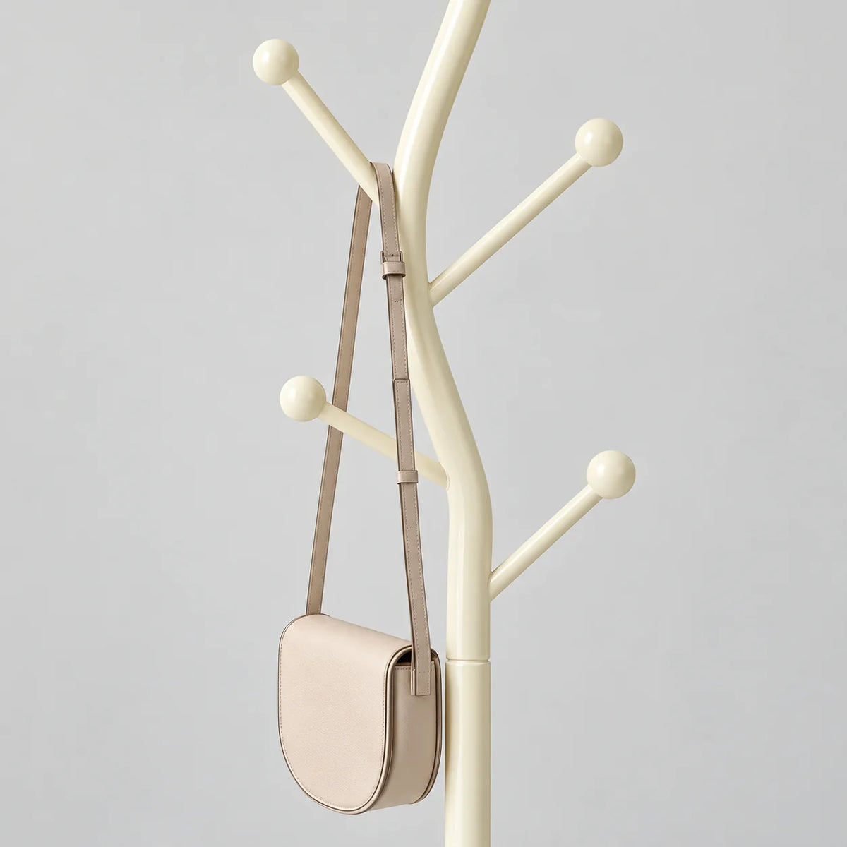 Détail des branches médianes et basses à boules du porte-manteau blanc crème et de son petit sac à bandoulière sur fond gris