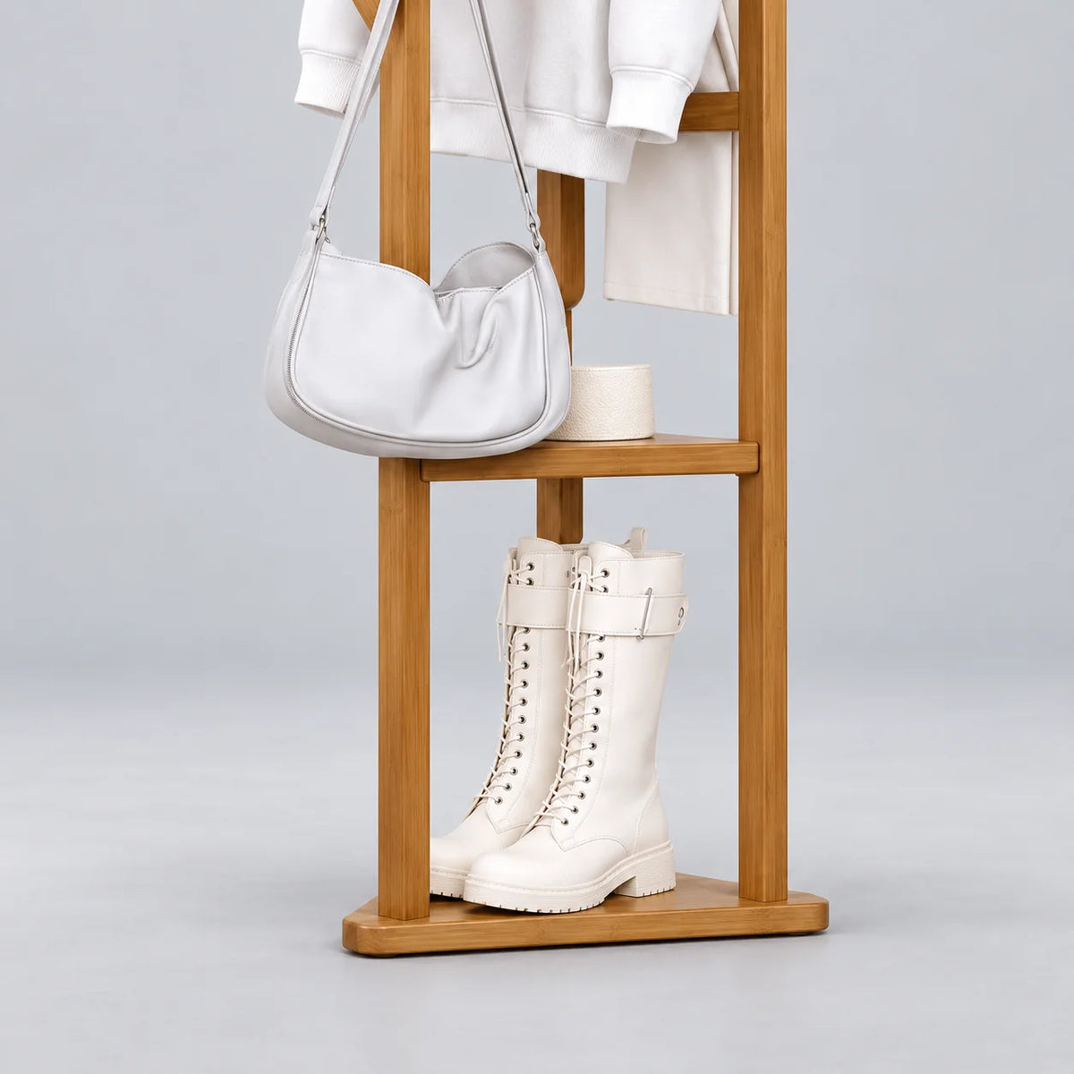 Gros plan du rangement inférieur du porte-manteau en bois clair avec une paire de bottes