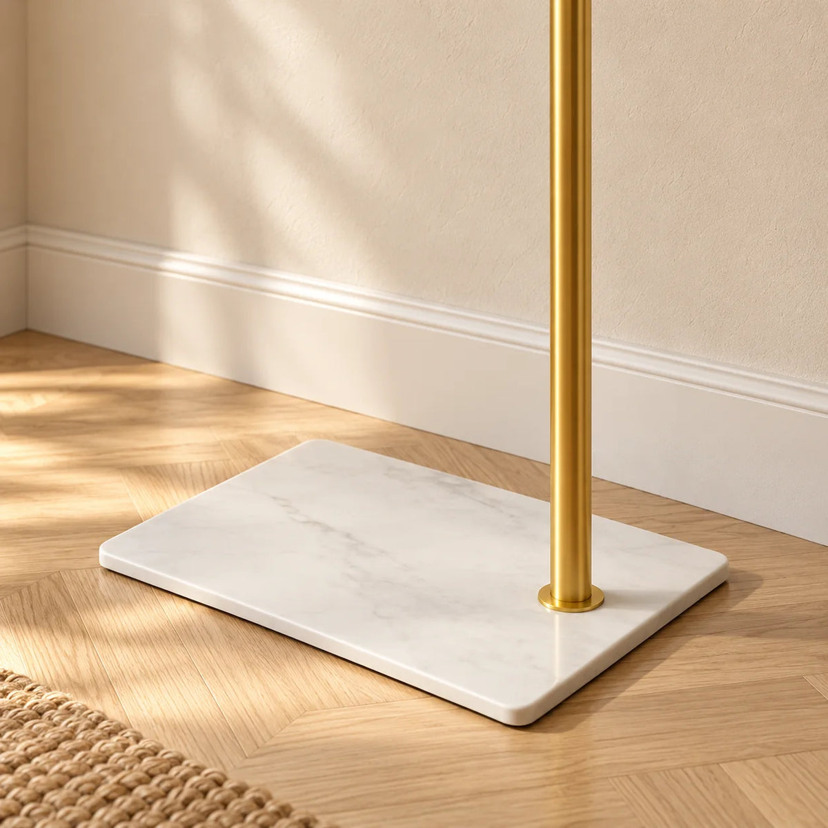 Gros plan du socle blanc légèrement marbré et de la tige dorée du porte-manteau voûté