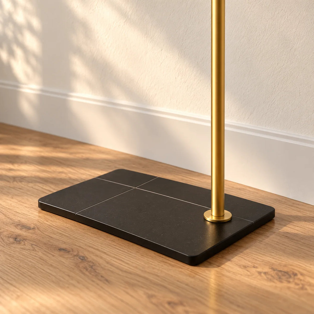 Gros plan du socle rectangulaire noir et de la tige dorée du porte-manteau voûte