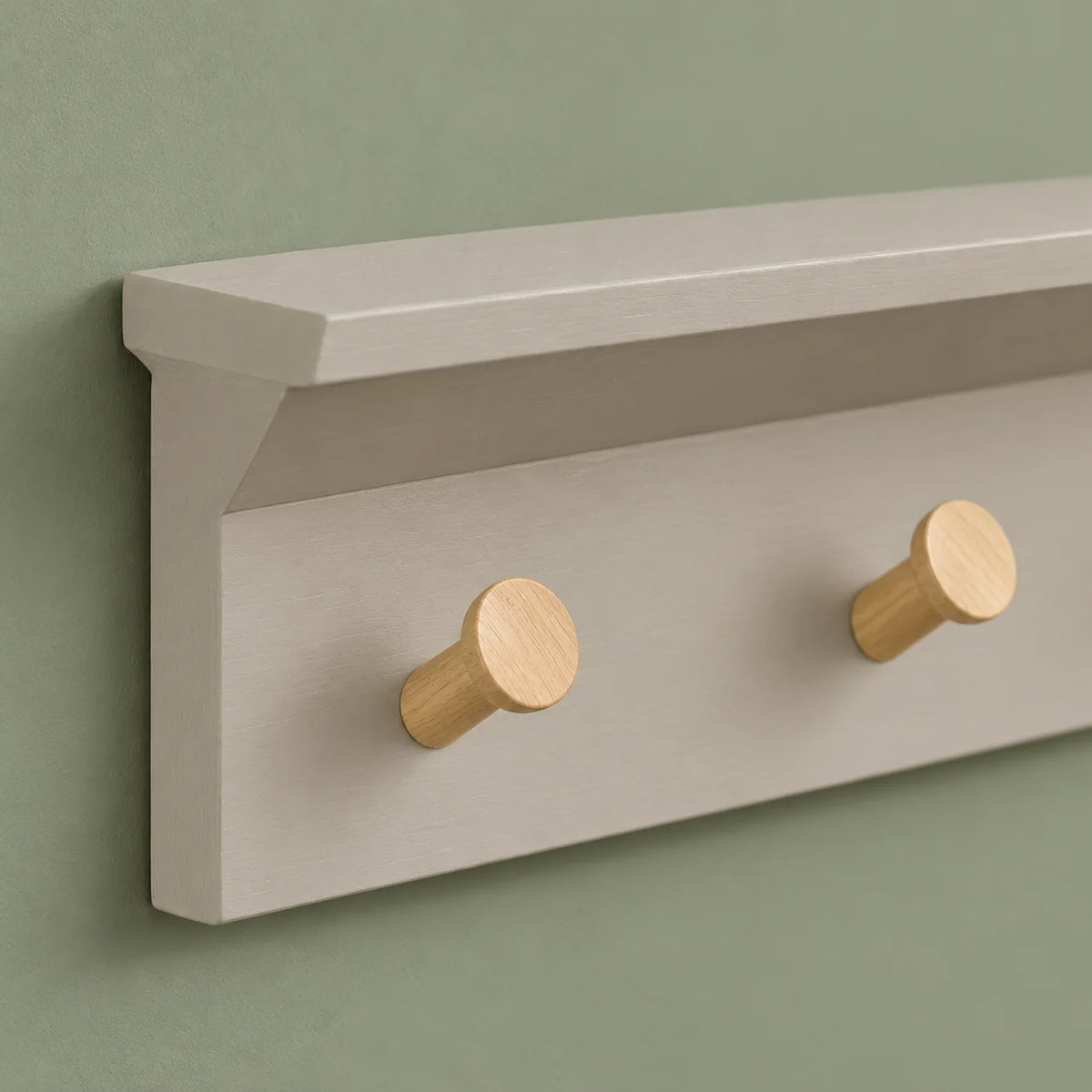 Détail des deux patères en bois naturel et de la tablette grise sur fond vert sauge