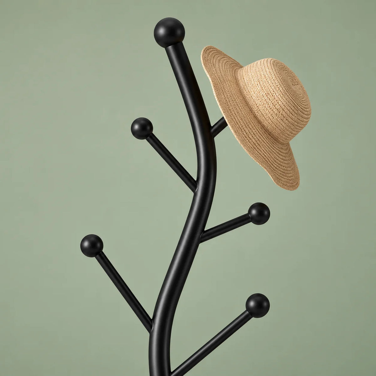 Détail du sommet incurvé noir mat et de ses crochets à boules avec chapeau de paille beige sur fond vert sauge