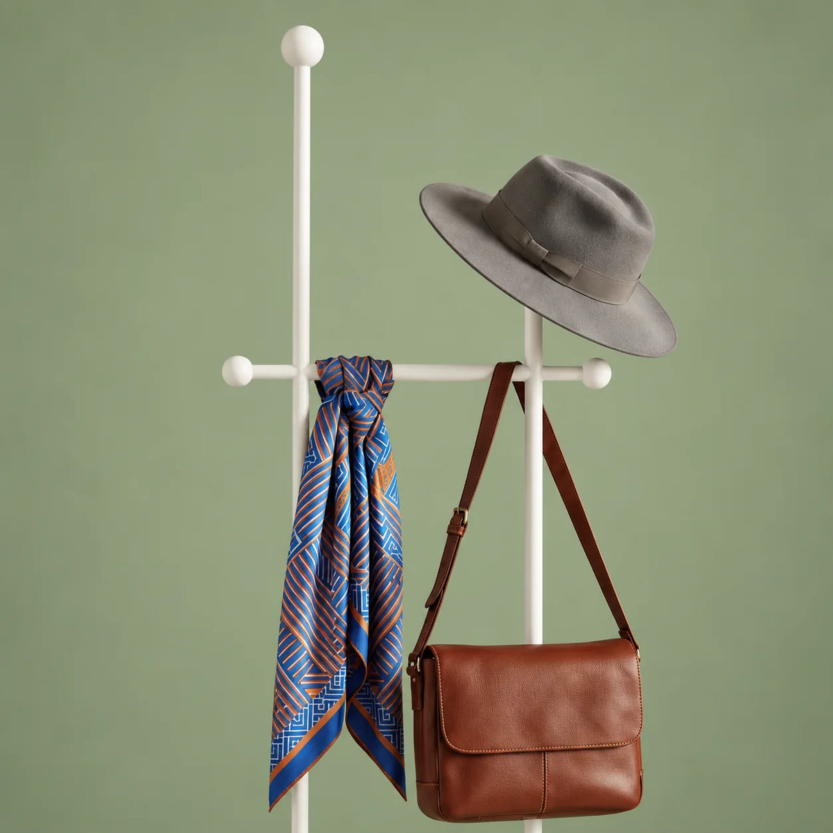 Détail des montants blancs, de la traverse à boules, du chapeau gris, du foulard et du sac brun sur fond vert sauge