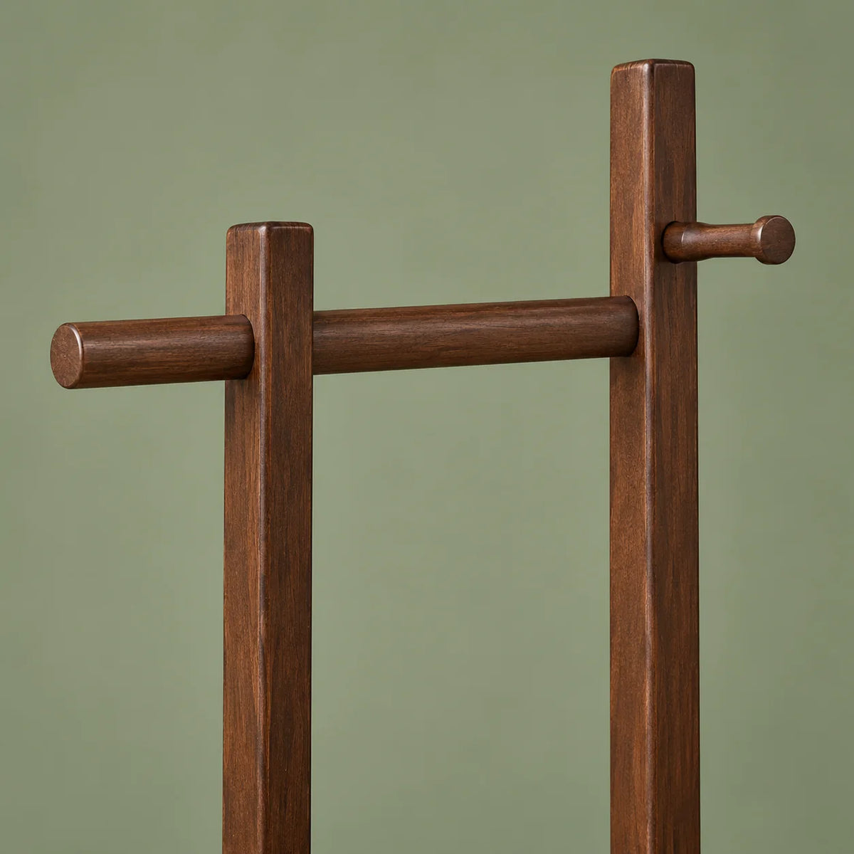 Détail de la barre haute et des crochets du porte-manteau en bois foncé sur fond vert