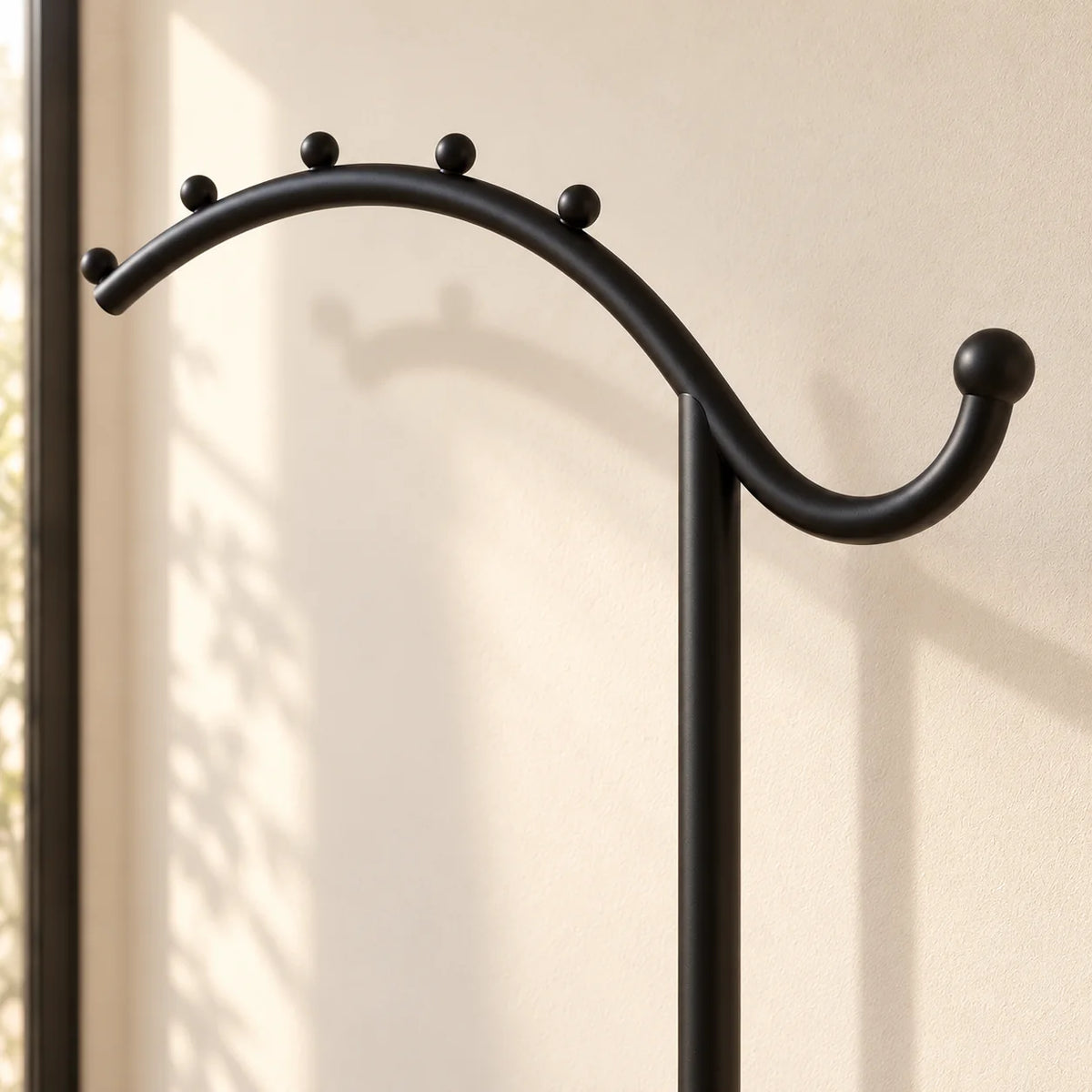 Détail de l’arceau noir et de ses crochets arrondis sur le porte-manteau voûté