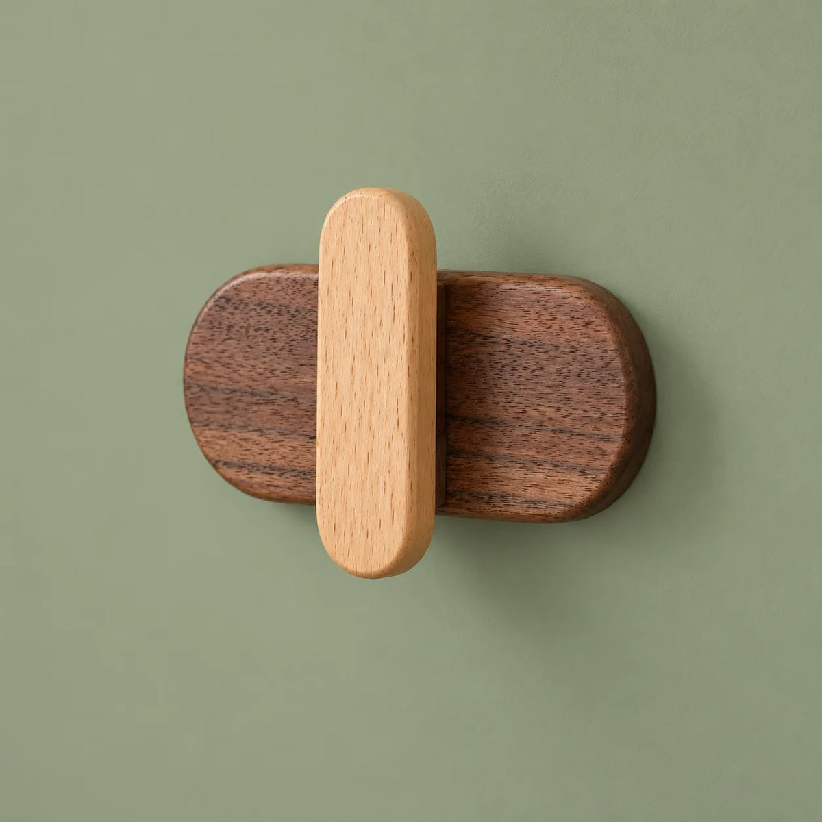 Patère capsule claire en bois foncé et clair sur un mur vert sauge