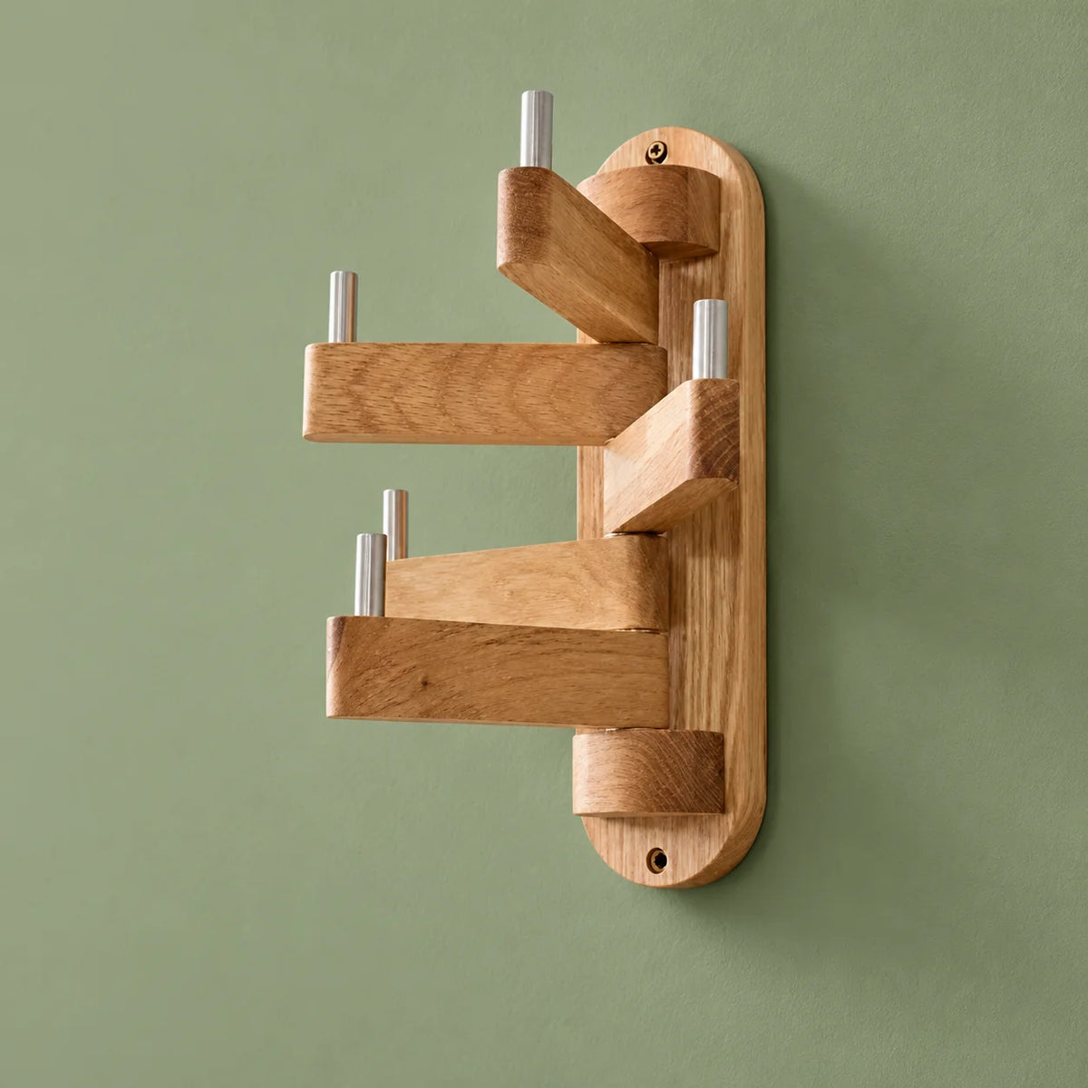 Porte-manteau mural pivotant en bois beige, cinq bras déployés sur fond vert sauge