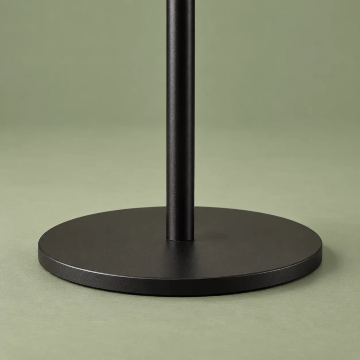 Détail de la base noire ronde du porte-manteau sur fond vert sauge