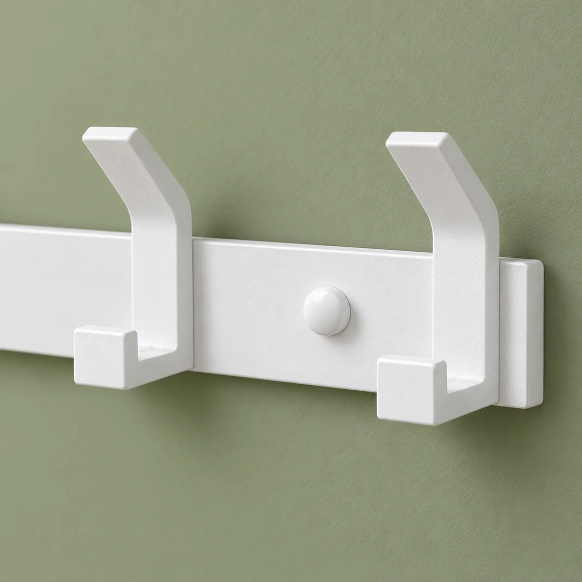 Détail des crochets de droite du porte-manteau blanc sur fond vert sauge