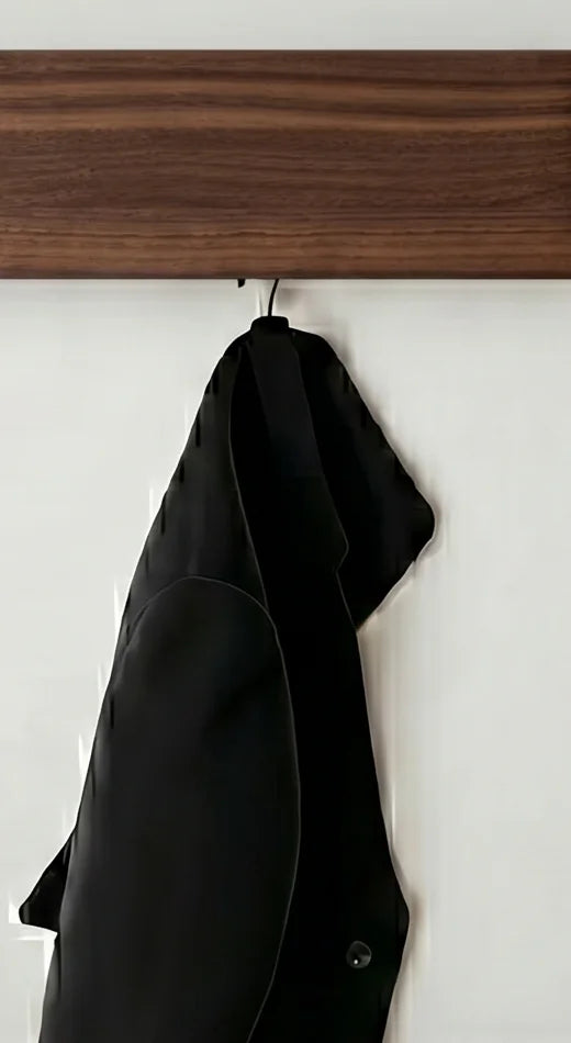 Détail de la patère sombre visible sous le panneau en bois foncé et du manteau noir suspendu