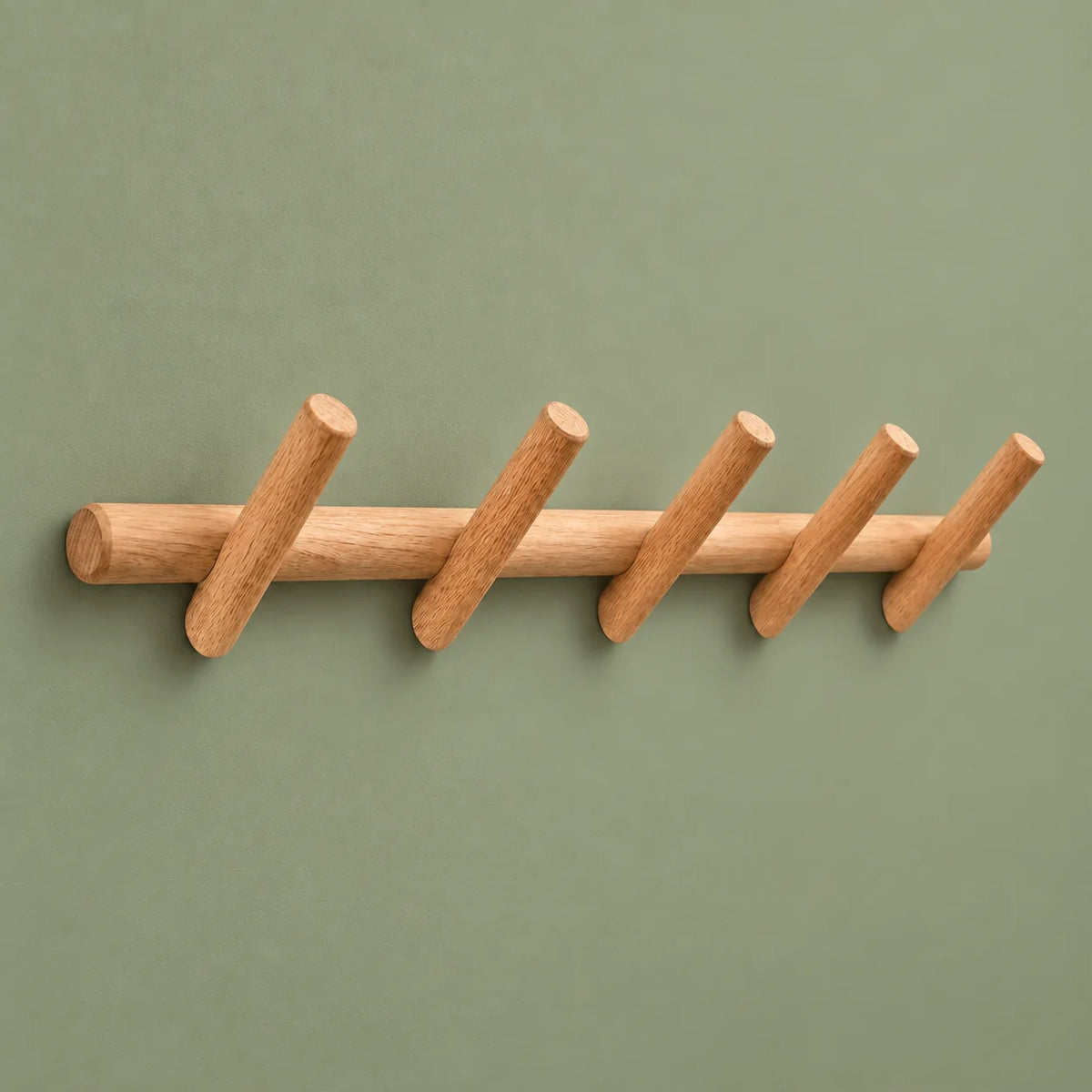 Porte-manteau mural en rondin de bois clair et cinq patères sur fond vert sauge
