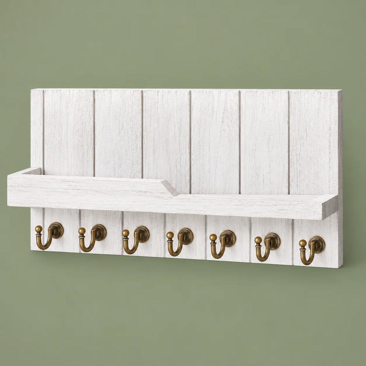Vue complète du porte-manteau mural blanc en bois avec sept crochets dorés sur fond vert sauge