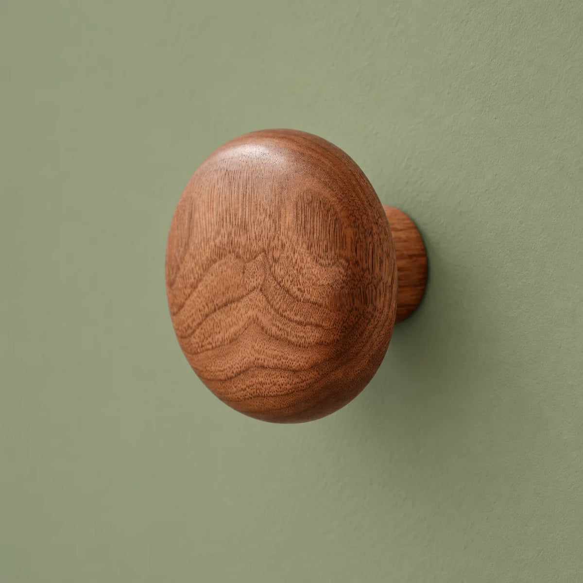 Patère ronde en bois brun foncé sur fond vert sauge