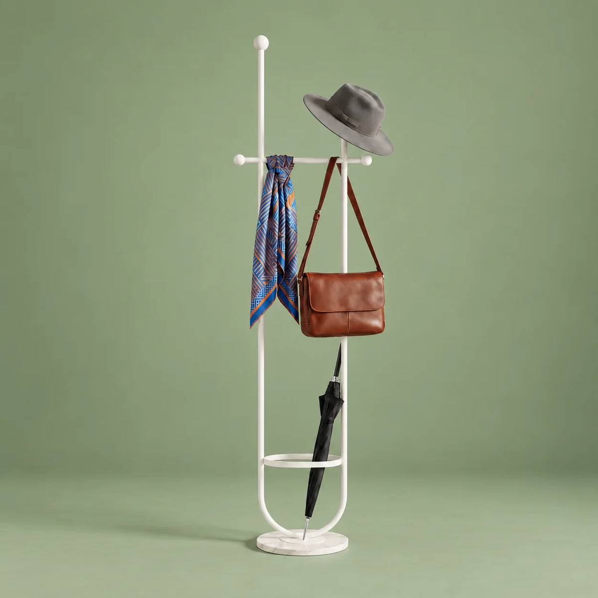 Porte-manteau sur pied en métal blanc avec chapeau, foulard, sac et parapluie, anneau porte-parapluie et base ronde blanche veinée sur fond vert sauge